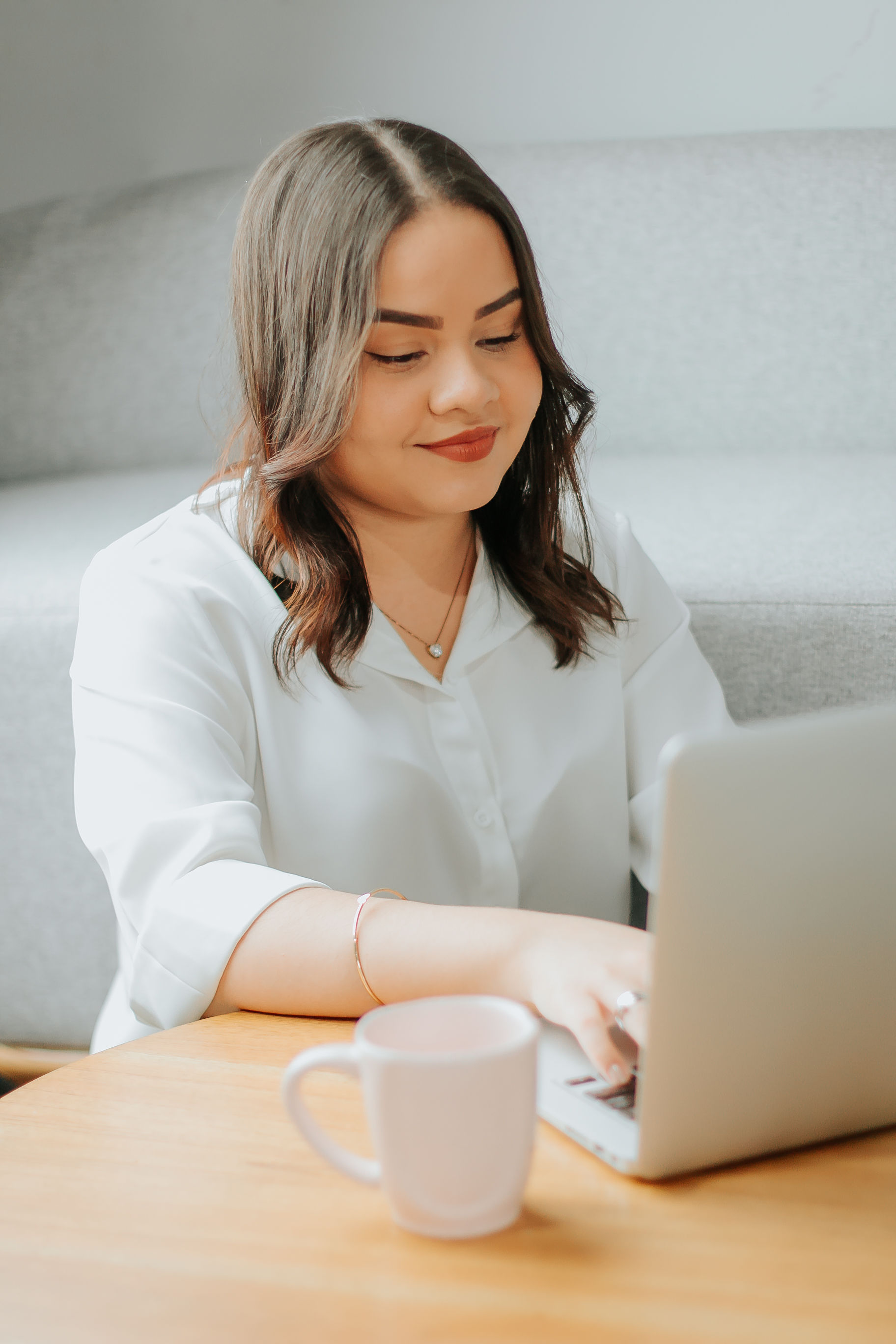 Mulher mexendo no notebook em uma mesa com uma xicara de café ao lado